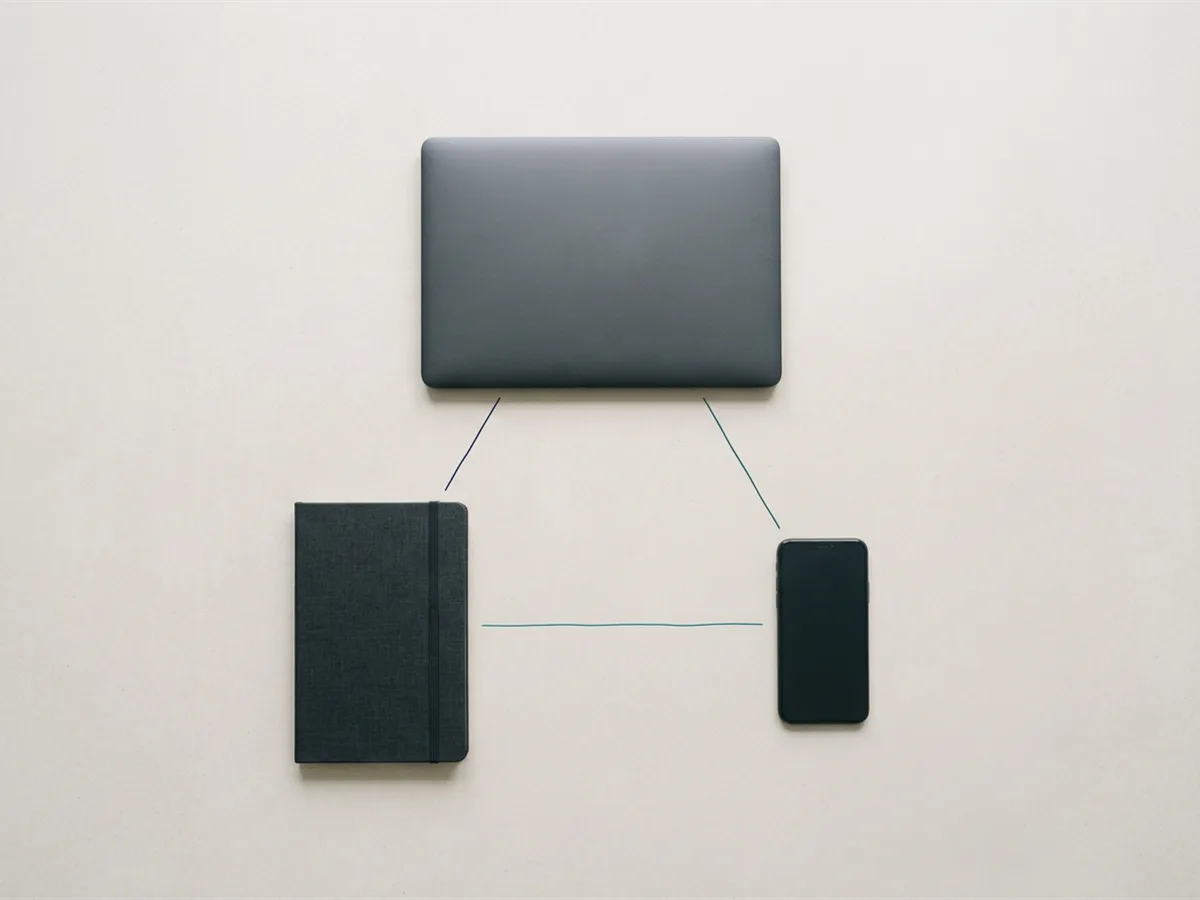 Minimalist flat-lay of connected system components including notebook, laptop and phone arranged to suggest integration